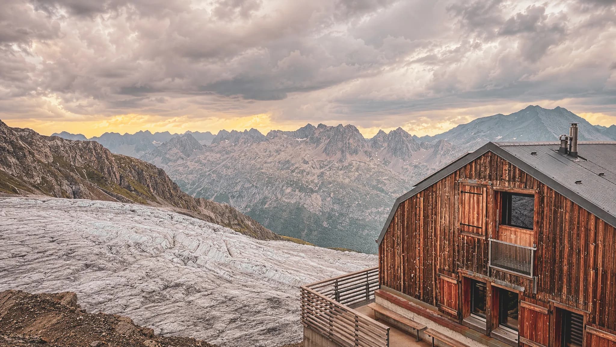 Magnifique paysage alpin avec un chalet en bois surplombant un glacier et des montagnes majestueuses.