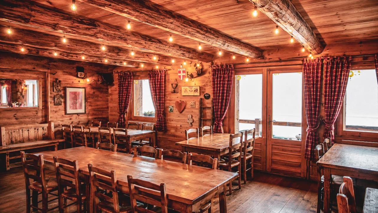 Petit chalet chaleureux en bois, tables en bois rustiques, éclairage chaleureux et rideaux à carreaux.