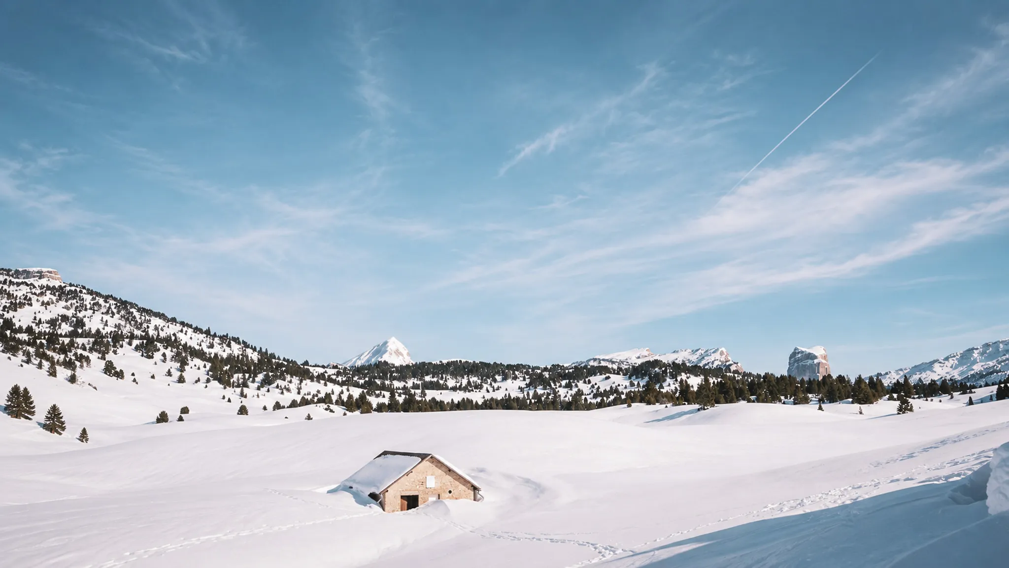 Un paysage hivernal splendide, avec une cabane en bois entourée de neige et montagnes majestueuses.