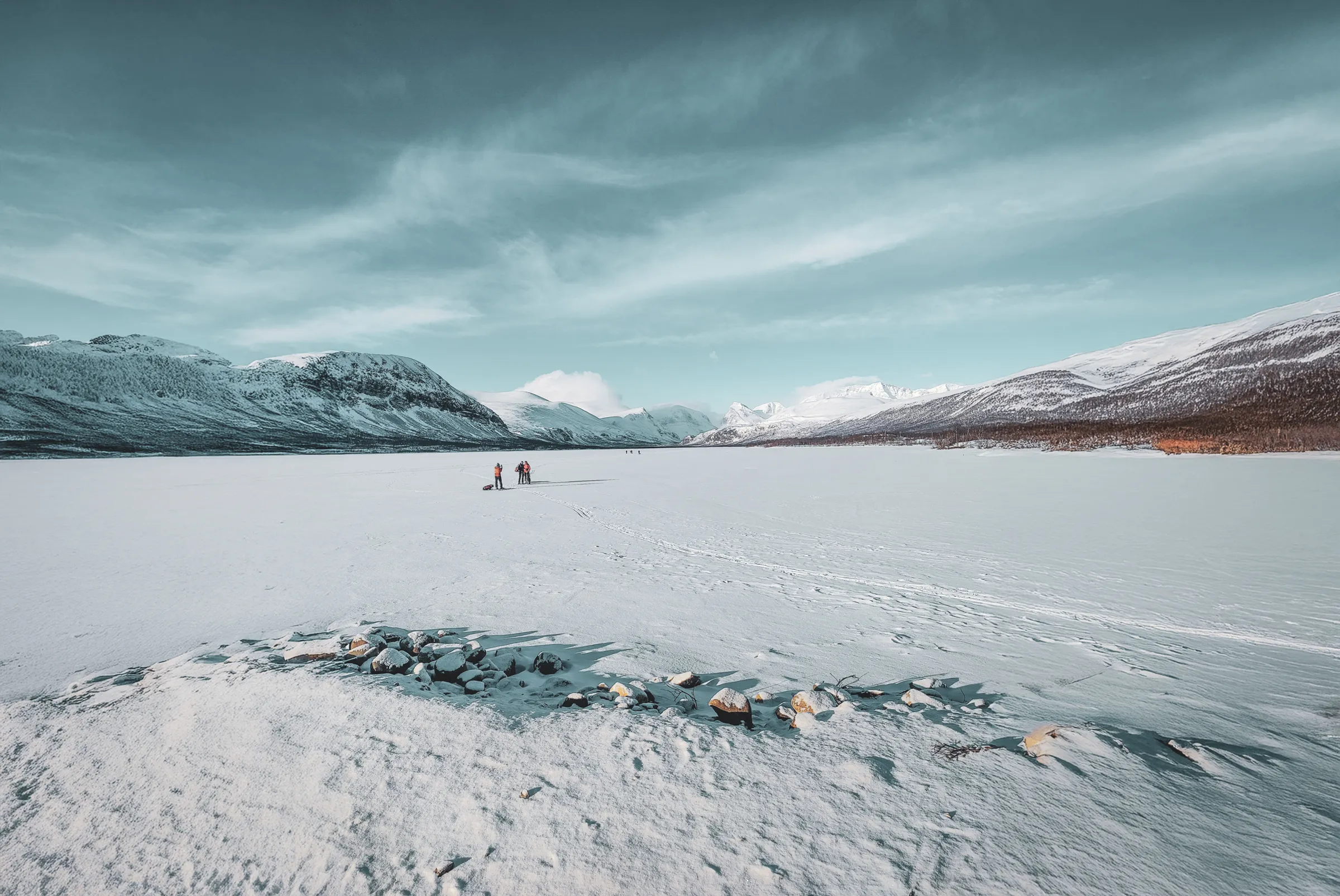 Scène hivernale magnifique sur le Kungsleden, avec randonneurs sur un lac gelé entourés de montagnes.