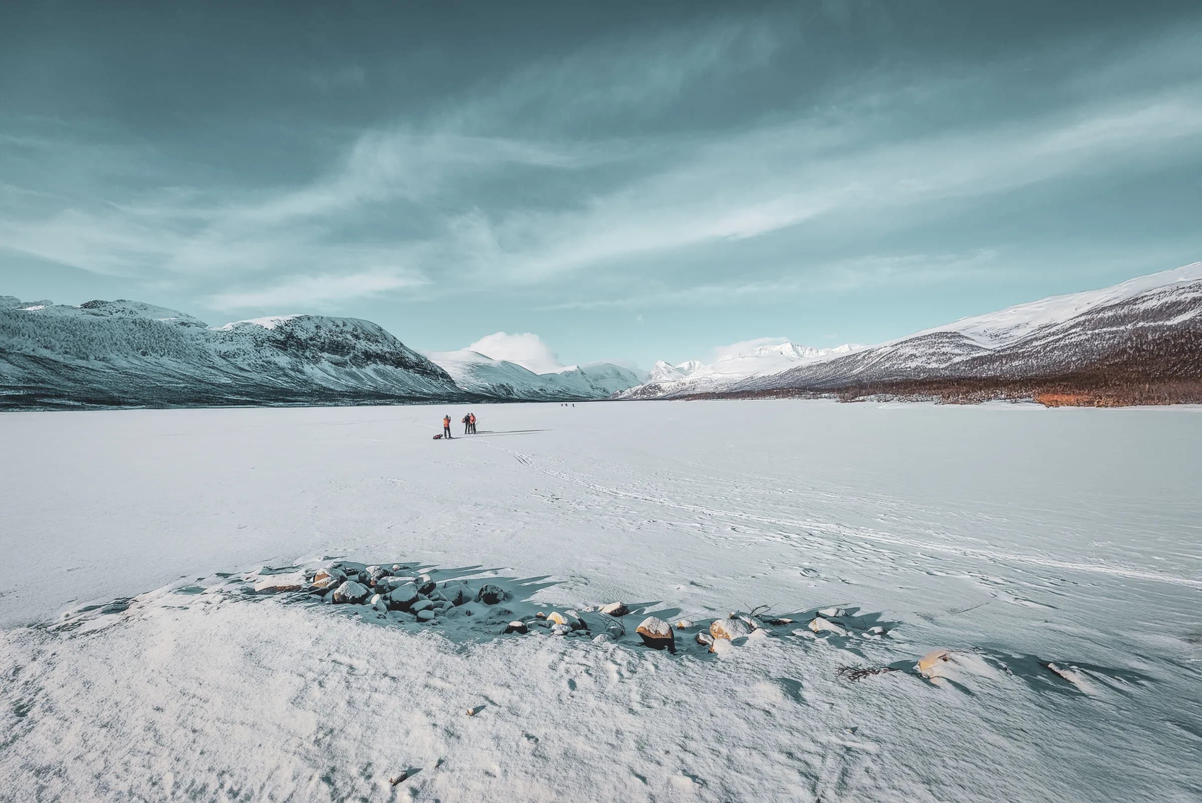 A magnificent winter scene on Kungsleden, with hikers on a frozen lake surrounded by mountains.