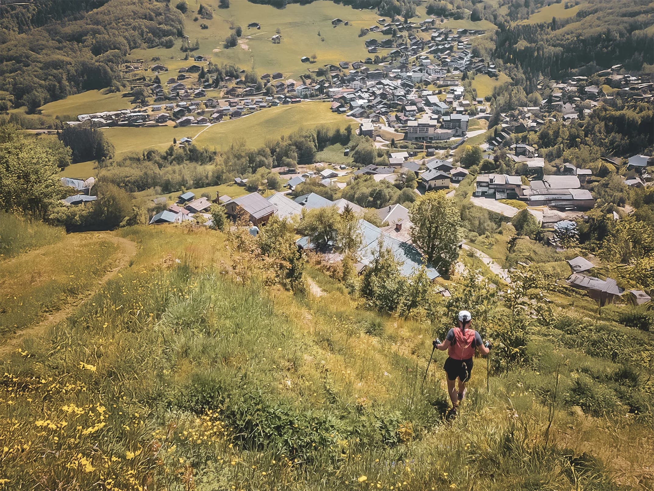 Een wandelaar daalt een groen pad af met uitzicht op een pittoresk dorpje in de Alpen.