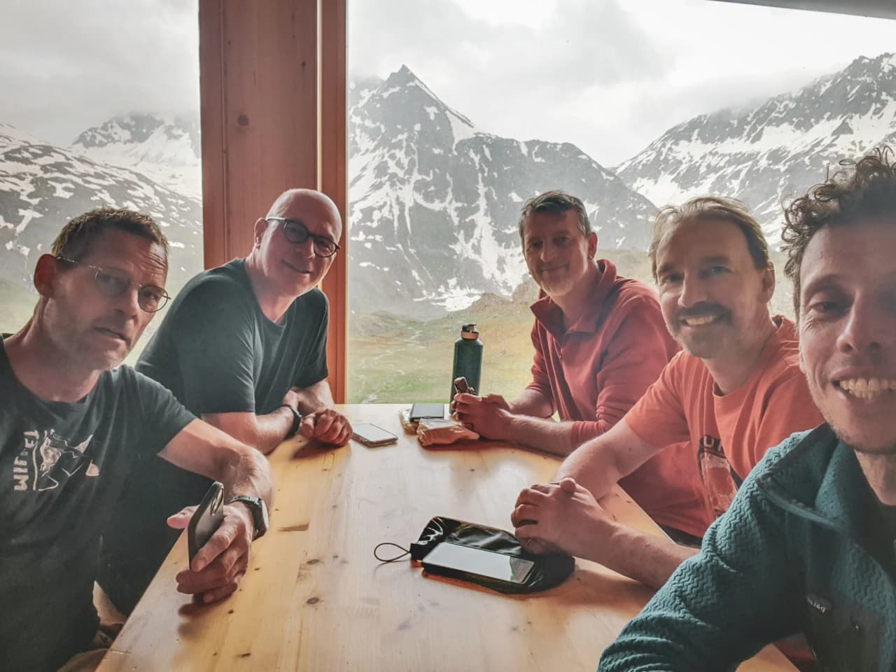 A group of five friends sharing a convivial moment with majestic mountains in the background.