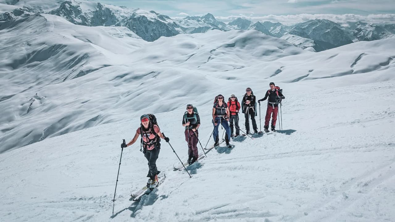 Un skieur solitaire trace des sillons sur une neige immaculée, face à des montagnes majestueuses.