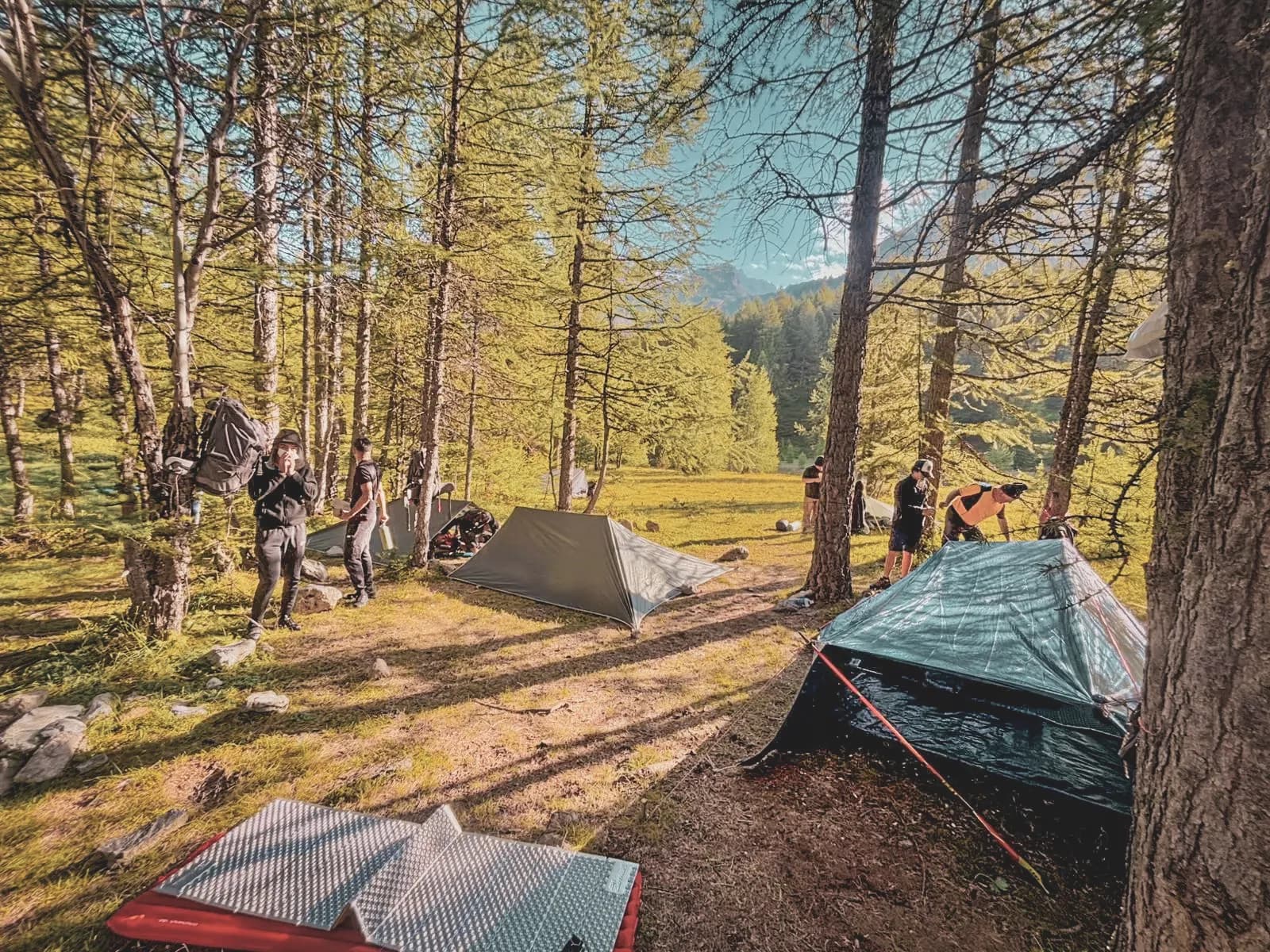 Groep in de open lucht, tenten opgezet, vriendelijke sfeer aan de voet van de Alpen.