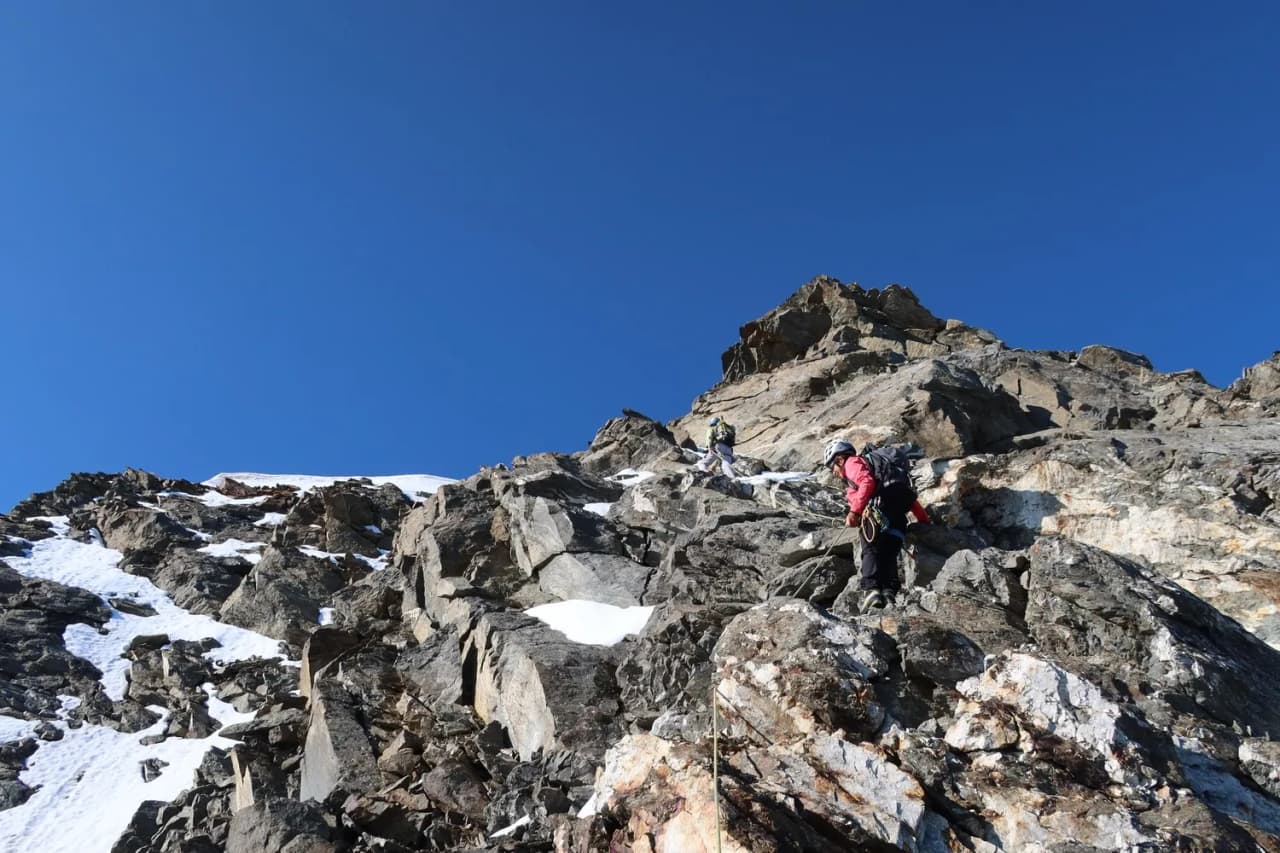 Mountaineers climbing steep rock under a blue sky, facing Mont Blanc. High mountain adventure!