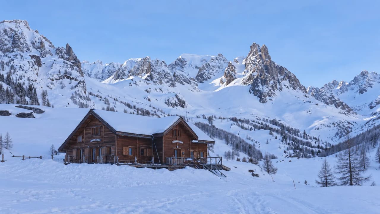A stylish timber building nestled amongst snow-capped mountains, an invitation to adventure in the Clarée Valley.