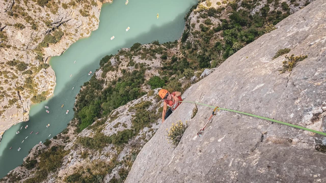 Een bergbeklimmer die een duizelingwekkende rotswand bedwingt, uitkijkend over het turkooizen water van de Gorges du Verdon.