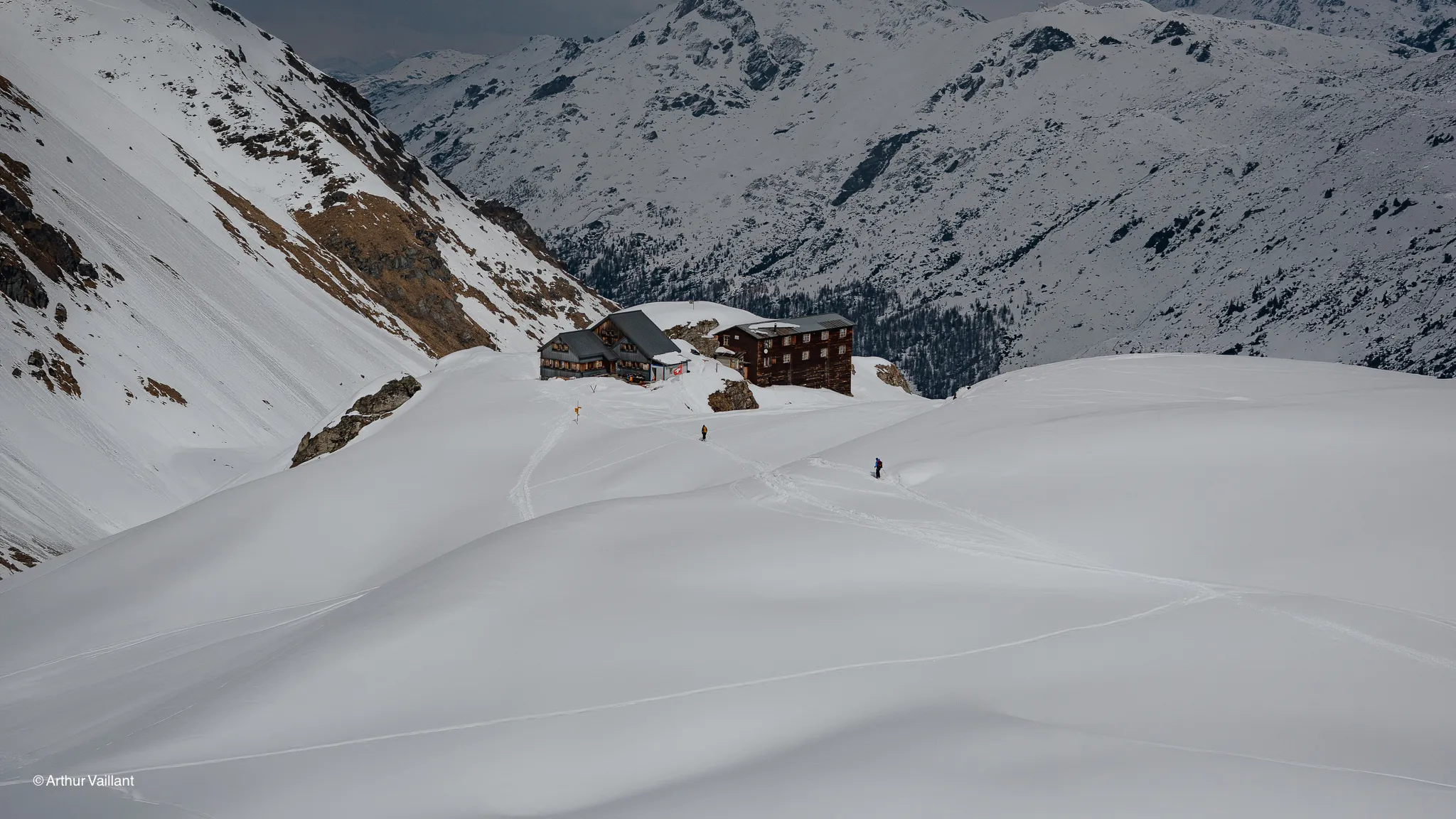 A spectacular Alpine view, with a chalet surrounded by snow-covered slopes and majestic mountains.