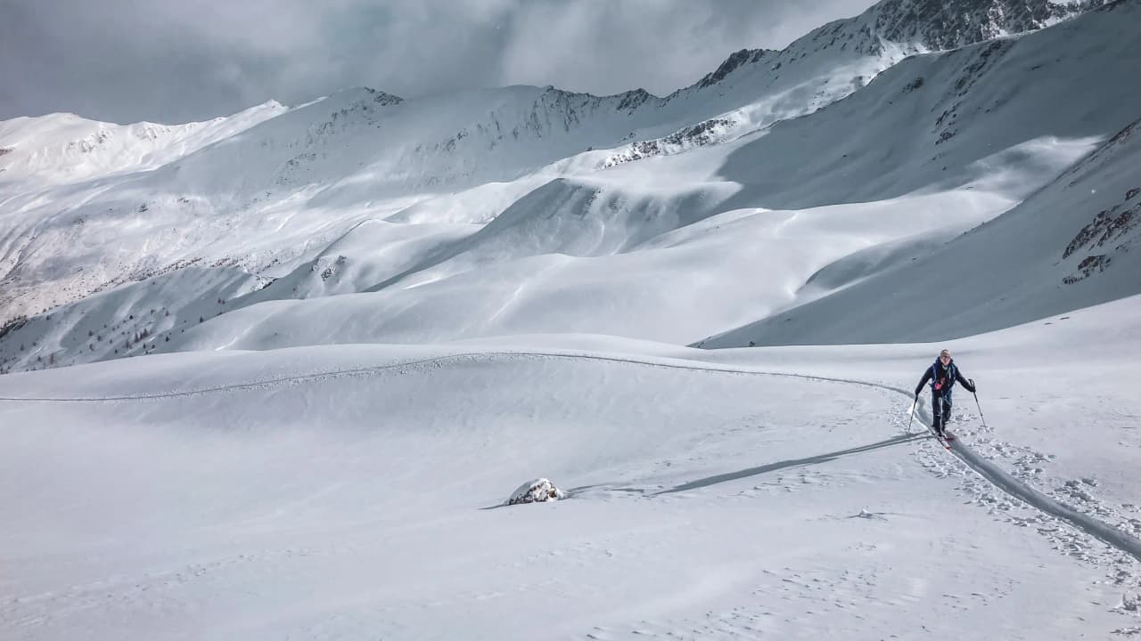 Un skieur solitaire évolue sur un vaste paysage enneigé, dominé par des montagnes majestueuses.