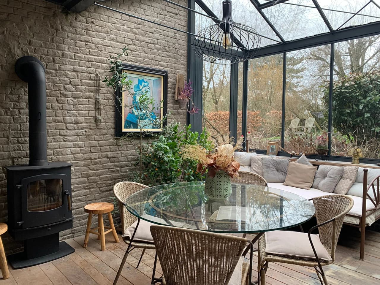 Light-filled relaxation area with wood-burning stove, green plants and views over the countryside, ideal for a Zen retreat.