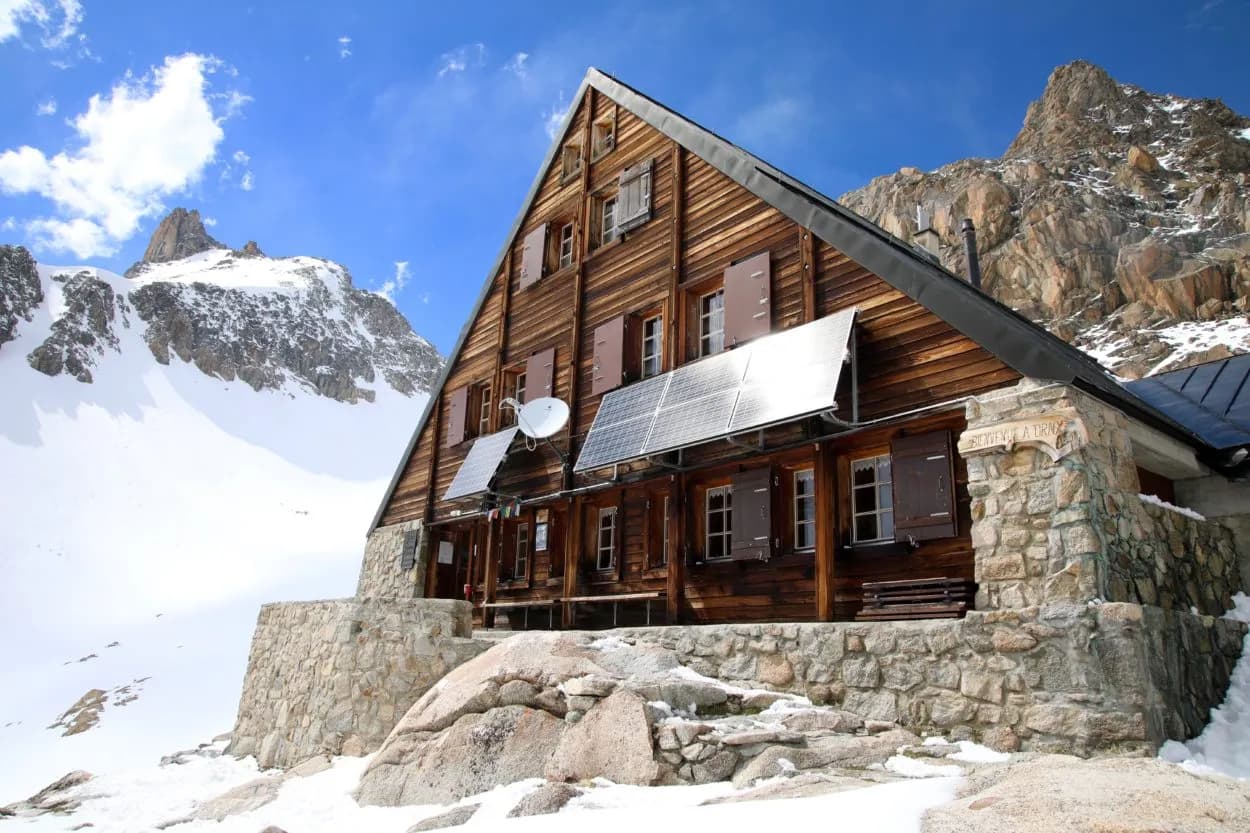 An Alpine wooden chalet, surrounded by snow-capped mountains, under a brilliant blue sky.