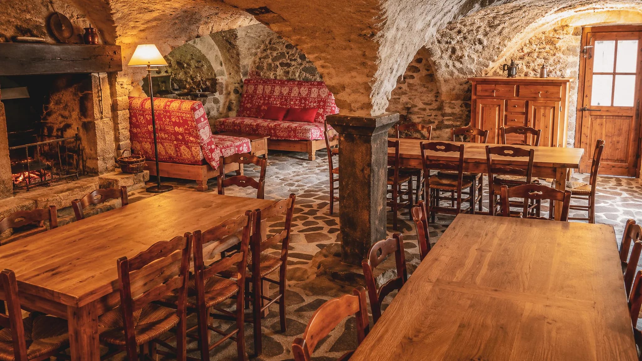 Een gezellig stenen interieur met open haard en houten tafels, ideaal om te ontspannen na een wandeling.