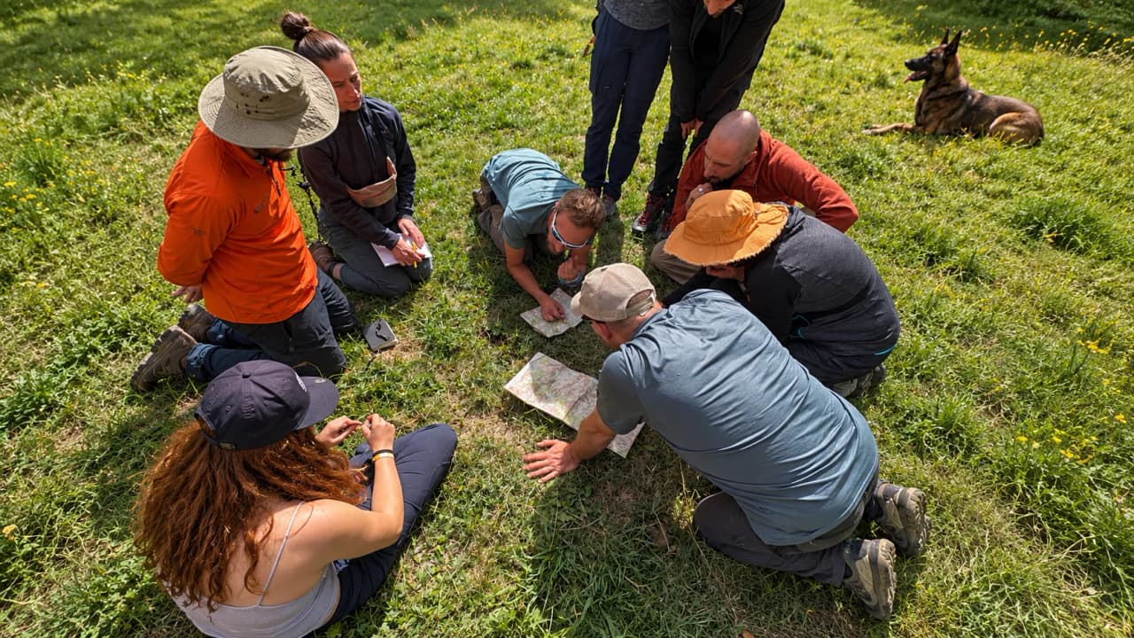 Groupe de personnes en pleine nature, étudiant une carte, entouré de verdure alpine.