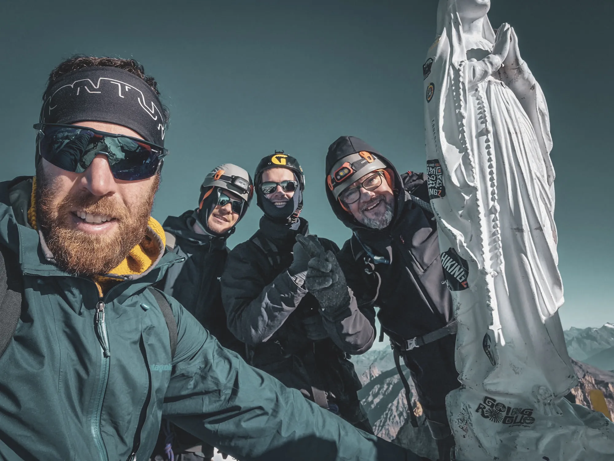 Four smiling climbers at the summit of Gran Paradiso, surrounded by majestic peaks.