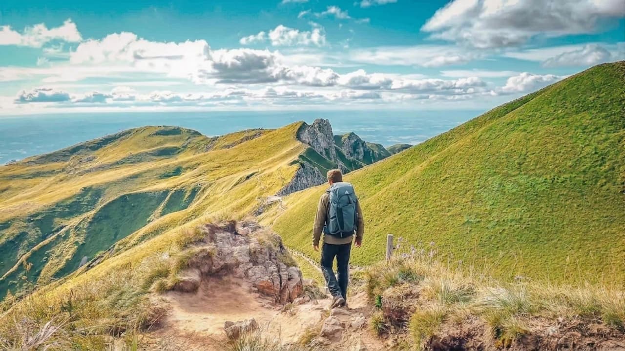 Wandelaar overdenkt de groene bergkammen en vulkaanlandschappen van het Centraal Massief.