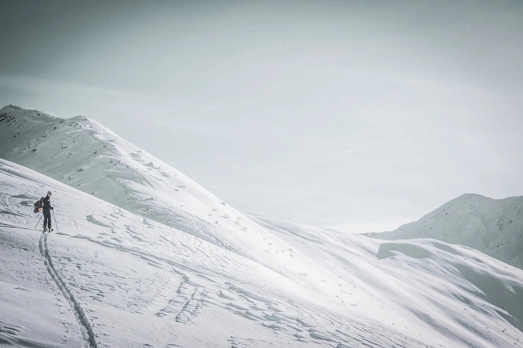 Lone skier climbing snow-covered slopes under a clear sky, enchanting Alpine panorama.