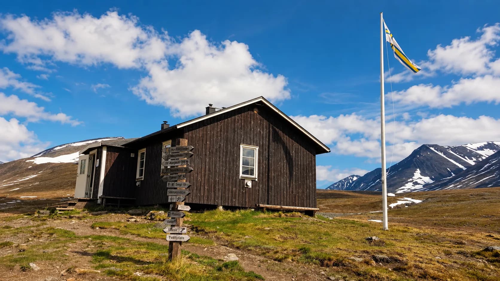 Een typisch houten hutje onder een blauwe hemel, omringd door besneeuwde bergen in Zweeds Lapland.