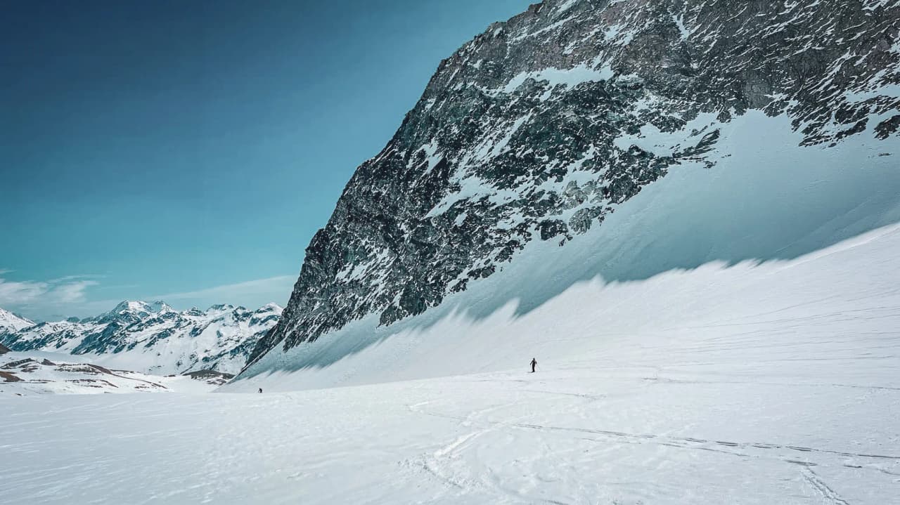 A solitary skier on a vast glacier beneath snow-capped peaks, an invitation to alpine adventure.