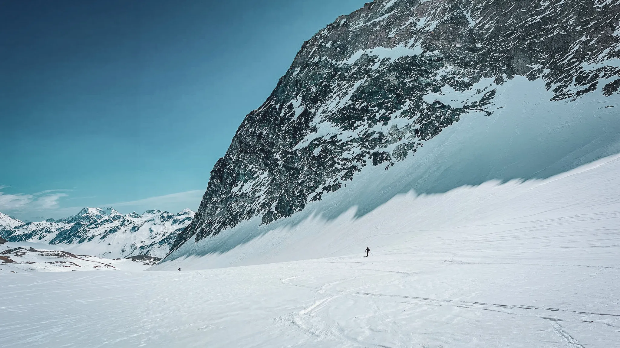 Un skieur solitaire sur un vaste glacier sous des sommets enneigés, invitation à l'aventure alpine.