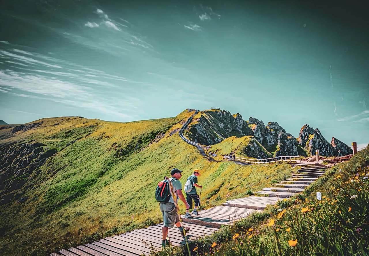 Twee wandelaars op een pad tussen de weelderige groene bergkammen van het Centraal Massief, heldere hemel.