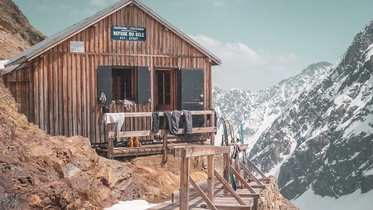 Refuge en bois au cœur des Écrins, avec vue sur montagnes enneigées et ciel bleu. Évasion garantie !